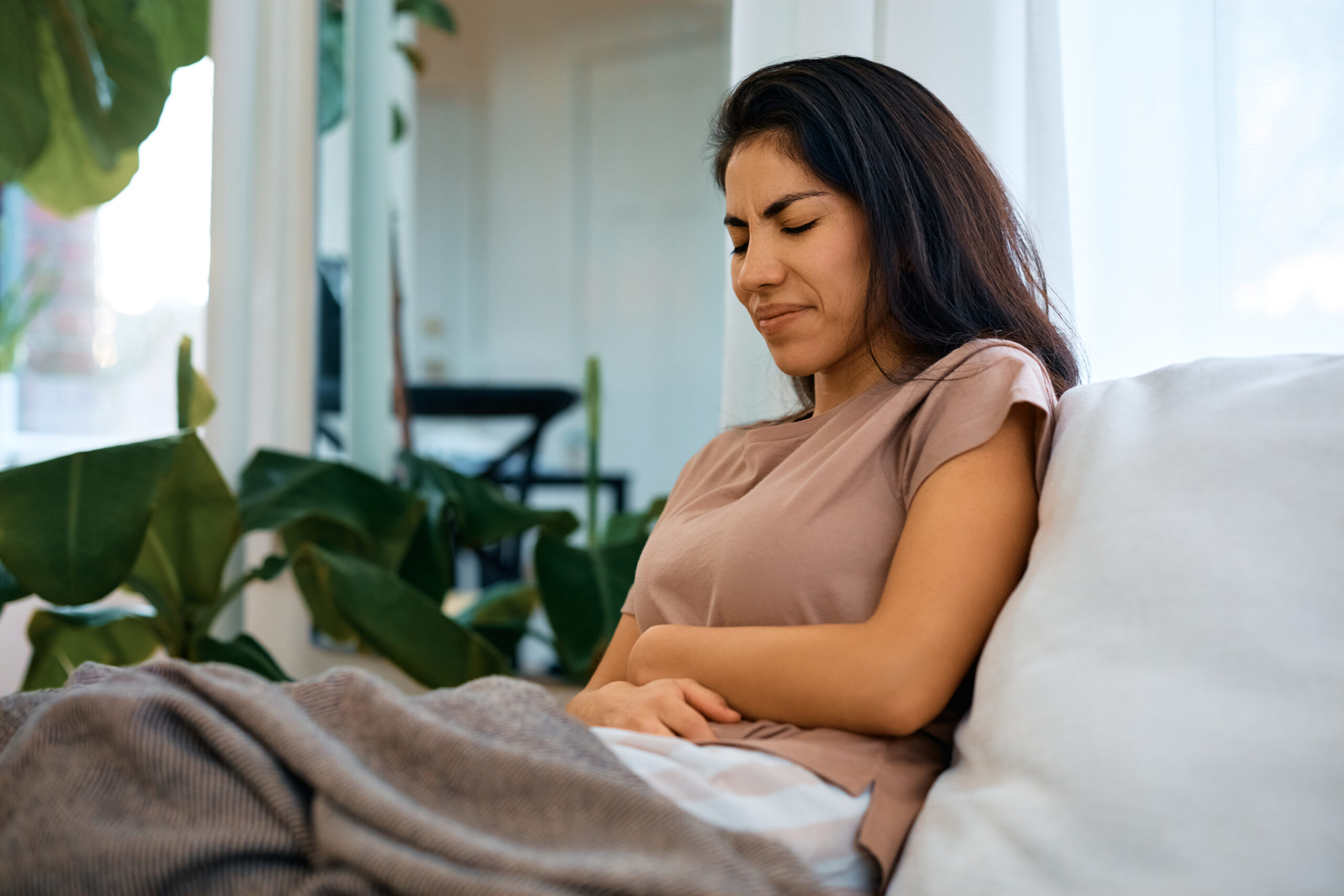 Mid adult woman suffering from stomach pain while sitting on sofa in the living room.